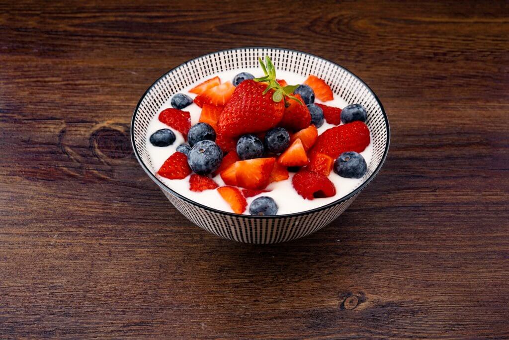 bowl of yogurt with strawberry and blackberries on top of brown table